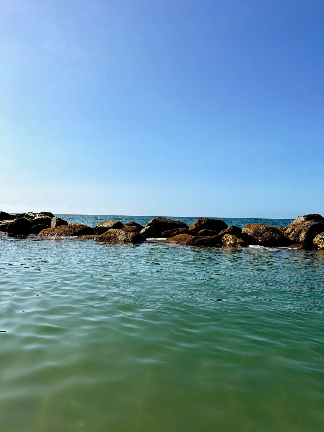 Calm sea and a rocky breakwater on a clear day, shot with Nōma's Khrome recipe